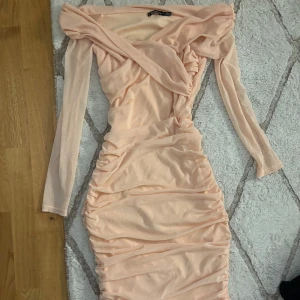 Ljusrosa omlottklänning med rynk - Supersnygg ljusrosa långärmad klänning från NA-KD med omlottdetalj upptill och rynkade partier längs hela klänningen. Klänningen har en figurnära passform och är gjord i mjukt, stretchigt material som sitter bekvämt. Perfekt för dig som vill sticka ut med en trendig look.