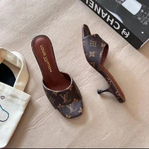 Louis Vuitton bruna klackar  - Säljer ett par lyxiga klackar Louis Vuitton med klassiskt monogrammönster i brunt och beige. Skorna har öppen tå, låg klack och en elegant, spetsig form. Materialet är skinn med LV-logga och blommor över hela ovandelen. Perfekt för dig som gillar designer och statement pieces. Helt nya och höjden på klacken är 5-6cm. Finns i storlek 35-40