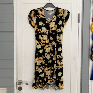 Svart blommig kortklänning - Supersöt svart klänning med gula och vita blommor. Kortärmad med v-ringning och volangkant nertill. Jätteskön passform då den är väldigt stretchig och skön i materialet. Köpt på barnavdelningen men passar mig utan problem som är 166cm lång o vanligtvis har xs.