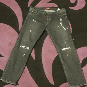 Svarta distressed jeans från Dsquared2 - Snygga svarta jeans från Dsquared2 i storlek 38. Jeansen har slitna detaljer och trasiga partier på benen för en riktigt edgy look. Klassisk femficksmodell med smal passform och låg midja. Perfekta för dig som gillar streetstyle och vill sticka ut.