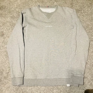  Les Deux tröja - Säljer en stilren ljusgrå sweatshirt från Les Deux i storlek XS. Tröjan har rund halsringning, diskret broderad logga på bröstet och ribbade muddar vid ärmslut och nederkant. Tillverkad i 100% bomull för en skön och mjuk känsla.