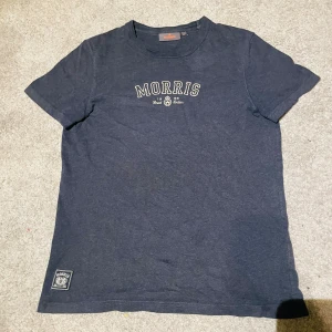 Morris tshirt - Snygg mörkblå t-shirt från Morris med klassisk logga tryckt på bröstet och en patch nertill. T-shirten har rund hals och är tillverkad i mjuk bomull, perfekt för en chill och stilren look.