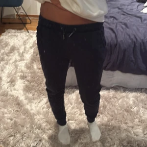 Svarta mjukisbyxor från FILA - Svarta mjukisbyxor från FILA med dragsko i midjan och smal passform. Byxorna har resår vid bensluten och en liten FILA-logga på ena benet. Perfekta för chill eller träning, tillverkade i mjukt material för maximal komfort.