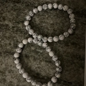 Vitt pärlarmband med marmormönster - Två elastiska armband med vita pärlor och grått marmormönster. Pärlorna är runda och ger en stilren och modern känsla. Perfekt accessoar för att lyfta din outfit med en cool detalj. 2 för 60kr