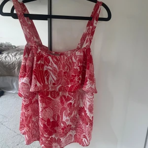 Rödvit blommig linnetopp från H&M - Säljer en röd och vit linnetopp från H&M i storlek 36. Toppen har breda axelband, volangdetalj framtill och ett snyggt blommigt mönster. Säljer pga av att den inte passar mig, så knappt använd 💕