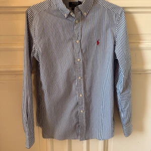 Randig Ralph Lauren skjorta - Snygg skjorta från Ralph Lauren med blå-vita ränder. Köpt på NK för ca. 2 år sen men knappt använd. I L barnstorlek (14-16), sitter typ som en XS i vuxenstorlek. Nypris 999kr