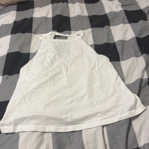 Vit ärmlös linnetopp från 157 - Säljer en vit ärmlös linnetopp från 157 med hög hals och snyggt skuren rygg. Toppen är i mjuk bomull och har en enkel, clean look som passar perfekt till jeans eller kjol. Perfekt för varma dagar eller lager på lager. Det är även två små snitt på sidorna av tröjan. En liten svart prick på framsidan men ingen som syns så mycket.
