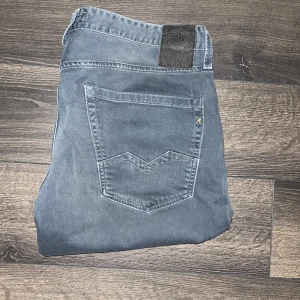 Replay Waitom jeans  - Snygga Replay Waitom jeans i blekt marinblå tvätt med klassisk femficksdesign och raka ben. Jeansen har diskreta slitningar och en svart patch bak i midjan. JAG SKICKAR INGA FLER BILDER ÄN DEN BEFINTLIGA NÄR JAG BÄR JEANSEN. Midja 45cm längd 98cm. Storleks lappen med L storleken saknas men den bedöms till L32 enligt mig men utgå från måtten :)