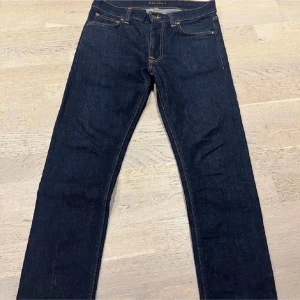 Mörkblå  jeans från Nudie Jeans (priset är inte hugget i sten) - Säljer ett par mörkblå  jeans från Nudie Jeans i klassisk femficksmodell. Jeansen har snygga kontrastsömmar och Nudie-logga på bakfickan. Tillverkade i slitstarkt denimtyg av bomull. Perfekt passform med smal siluett.