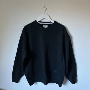 Blå sweatshirt från Converse Chuck Taylor - En blå sweatshirt från Converse Chuck Taylor med klassisk rund hals och ribbade muddar. Tröjan har en enkel och clean design med diskret Converse-logga nertill. Perfekt för en chill och avslappnad stil. 3S16