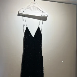 Svart lång paljettklänning - S - Supersnygg svart långklänning med tunna axelband, djup v-ringning och öppen rygg. Klänningen är täckt av glittriga paljetter och har en elegant, figurnära passform. Perfekt för dig som vill sticka ut och glänsa. Den är super bekväm och stretchig använd 1 kväll 