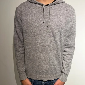 Grå kashmirhoodie från Sayless - Mjuk och lyxig grå hoodie från Sayless i kashmir. Klassisk modell med huva och snörning, ribbade muddar och lång ärm. Perfekt för dig som vill ha en stilren och bekväm tröja med premiumkänsla.