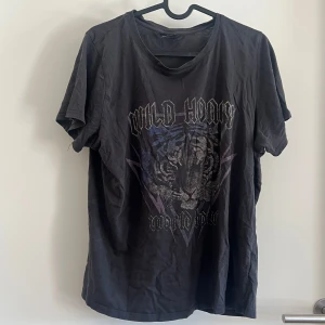 Svart t-shirt med tigertryck - Svart t-shirt från Gina Tricot i storlek L med tryck av tiger och texten 'Wild Honey World Tour' framtill. 