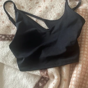 Svart linnetopp med cut out från H&M storlek XXS - Svart linnetopp från H&M Divided i storlek XXS. Toppen har smala justerbara axelband och en snygg cut out-detalj vid halsringningen. Tillverkad i mjuk och stretchig polyester som sitter tight och bekvämt. Perfekt för att lyfta din outfit med en cool touch.