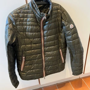 Moncler Daniel olivgrön - Säljer en Moncler Daniel i en olivgrön färg. Storlek 4.  Jackan är köpt 2020 och men har endast hängt i en garderob senaste 3-4 åren. Jackan är i fint skick med undantag för en liten 1.5cm reva på ryggen. Alla dragkedjor fungerar som de ska.   Bara att skriva om du vill ha fler bilder eller liknande!
