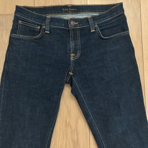 Nudie jeans - Snygga mörkblå jeans från Nudie Jeans med klassiska kontrastsömmar och femficksdesign. Jeansen har en smal passform och är tillverkade i slitstarkt denimtyg av bomull. Bakfickorna har Nudie Jeans ikoniska broderi.