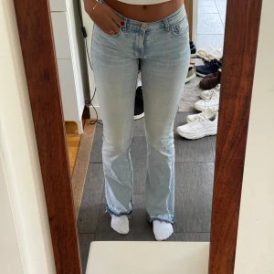 Ljusblå bootcut jeans  - Säljer ett par ljusblå bootcut jeans med låg midja och rå, fransig kant nertill. Jeansen har klassisk femficksdesign och är tillverkade i mjukt denimtyg. 
