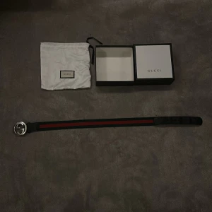 Gucci bälte med GG-spänne - Säljer ett klassiskt Gucci bälte med ikoniskt GG-spänne i silverfärgad metall. Bältet har gröna och röda ränder längs hela bandet och detaljer i brunt skinn. Kommer med originalpåse och ask. Perfekt accessoar för att lyfta din outfit.
