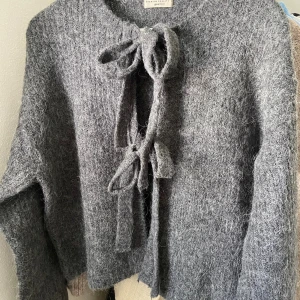 Grå stickad kofta från Gina Tricot - Mysig grå stickad kofta från Gina Tricot med två knytband framtill. Koftan har lång ärm och tjockt material! Perfekt till vintern eller hösten!! Skriv för mer bilder eller frågor!