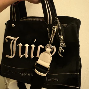 Juicy Couture Väska Oanvänd  - Ikonisk Juicy Couture-väska i svart sammet med beige brodyr - äkta, oanvänd! Tillhörande beige mini pouch med ”In Juicy We Trust”-detalj ingår. Köpt på Raglady.