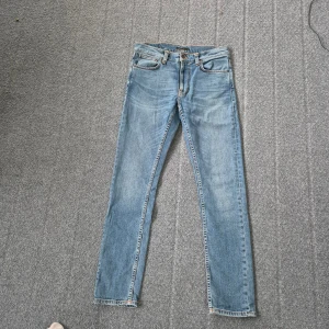 Nudie Jeans Lean Dean ljusblå jeans - Säljer ett par Nudie Jeans Lean Dean i ljusblå tvätt, modell Lost Orange. Jeansen har klassisk femficksdesign, orangea sömmar och är tillverkade av 99% ekologisk bomull och 1% elastan för extra stretch. Snyggt smal passform och raka ben. Ser lite ljusare ut på bild än vad de är.
