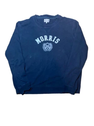 Morris marinblå college-tröja - Snygg marinblå college-tröja från Morris med klassiskt tryck och emblem på bröstet. Tröjan har rund halsringning och långa ärmar. Tillverkad i mjuk bomull som är skön att bära. Perfekt för en avslappnad och stilren look.