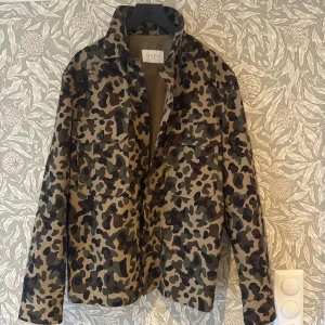 Camouflage overshirt från Sandro Paris - Säljer en riktigt snygg overshirt från Sandro Paris i camouflage-mönster. Jackan har två stora bröstfickor med knappar, klassisk krage. Perfekt för dig som vill sticka ut med en sjukt snygg overshirt! STORLEK M, Nypris 3799kr 