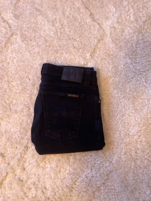 Mörkblå jeans från Nudie Jeans - Snygga svarta jeans från Nudie Jeans med klassisk femficksdesign och subtila sömmar på bakfickorna. Modellen är slim och är tillverkad i mjukt jeansmaterial med stretch för extra komfort. Perfekt för dig som gillar stilrena och tidlösa jeans.