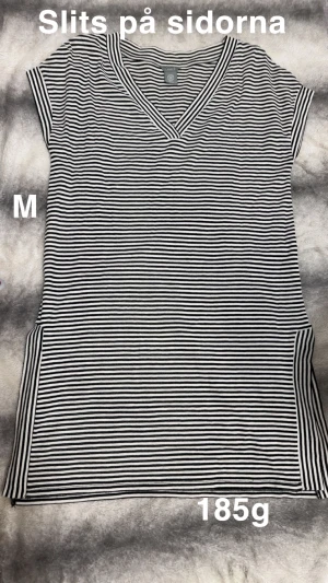 Randig svartvit v-ringad tunika M - Säljer en svartvit randig tunika från Lindex i storlek M. Tunikan har v-ringad hals, korta ärmar och slits på sidorna för extra rörelsefrihet. Perfekt för dig som gillar enkel och stilren design. 🌸.