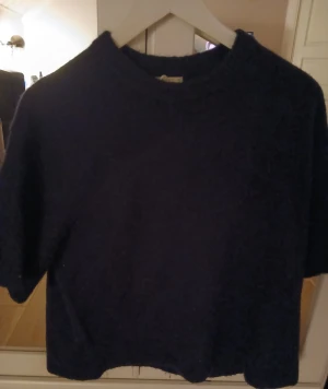 Mörkblå stickad t-shirt Gina Tricot - Snygg mörkblå stickad t-shirt från Gina Tricot i storlek M. Modellen har korta ärmar, rund hals och en loose passform. Materialet är mjukt och stickat, perfekt för dig som gillar en chill och enkel stil.