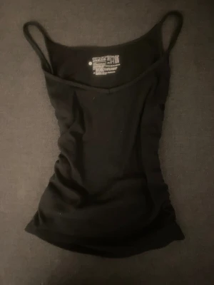 Svart ribbad linnetopp  - En svart ribbad linnetopp med smala axelband och figurnära passform. Perfekt att styla med jeans eller kjol för en enkel och snygg look. Materialet är mjukt och stretchigt för extra komfort.
