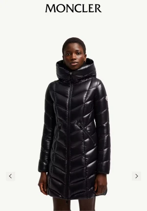Svart Moncler dunjacka med huva - Marus Hooded Jacket - Säljer en svart, lång dunjacka från Moncler med snygg glansig finish och huva. Jackan har quiltad design i V-mönster, två fickor med dragkedja och Moncler-logga på ärmen. Perfekt för kalla dagar och har en riktigt clean look. STORLEK M passar även L