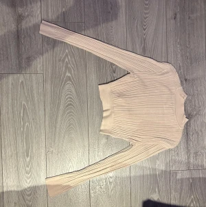Beige ribbad tröja  - Säljer en beige ribbad stickad tröja från new yorker med lång ärm och tight passform. Tröjan har en högre halsringning och bred mudd nedtill som ger en snygg siluett. Perfekt att styla med jeans eller kjol för en clean look.