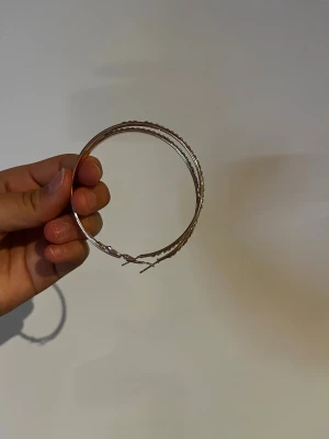 Stora silvriga hoops med stenar - Säljer ett par stora, runda örhängen i silverfärgad metall med glittrande stenar längs hela framsidan. De har klassisk hoop-form och stängs med enkel låsning. Perfekta för dig som gillar att sticka ut med accessoarer som glittrar.
