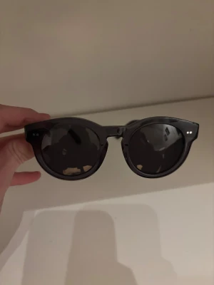 Svarta solglasögon från Chimi - Snygga svarta solglasögon från Chimi med rundade bågar och mörka linser. Ramen är i blankt acetat och har två små silvriga detaljer vid sidan av fronten. Perfekt accessoar för att lyfta din stil.