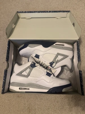 Nike Air Jordan 4 Midnight Navy - Säljer ett par Nike Air Jordan 4 i vitt och mörkblått med grå detaljer. Skorna har klassisk mesh på sidorna, speckled grå midsole och Jumpman-logga på plösen. Tillverkade i skinn och syntet, med snörning och platt sula. Riktigt clean och ikonisk siluett för dig som gillar sneakers.