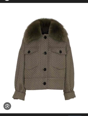 Beige overshirt med pälsdetalj - Snygg beige meotine jacka. Jackan har stora fickor framtill, svarta knappar och långa ärmar med breda muddar. Perfekt för dig som vill ha en unik och trendig look med extra detaljer.