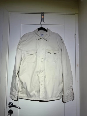 Beige overshirt från Sams - Snygg beige overshirt från Sams i bomull med klassisk krage och två bröstfickor med lock. Långärmad modell med knappar framtill och vid ärmslut. Perfekt att slänga på över en t-shirt för en chill look.