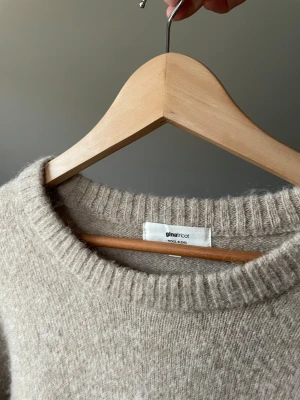 Beige stickad tröja från Gina Tricot - Mysig beige stickad tröja från Gina Tricot med rund hals och ribbade muddar vid ärmslut och nederkant. Tröjan är tillverkad i en mjuk ullblandning och har en klassisk, loose passform som är perfekt för kyliga dagar.