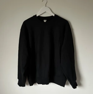 Svart sweatshirt från ARKET, M - En stilren svart sweatshirt från ARKET i storlek M. Tröjan har oversized fit, rund hals, långa ärmar och ribbade muddar vid ärmslut och nederkant. Tillverkad i mjukt material, perfekt för en chill och enkel look. Passar dig som gillar minimalistisk stil. 5N15