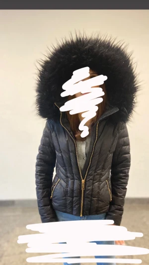 Svart pufferjacka Rockandblue - Säljer en svart pufferjacka från Rockandblue med stor fluffig huva och guldfärgade dragkedjor. Jackan har quiltad design, lång ärm och snygga detaljer som markerar midjan. Perfekt för kalla dagar och har en cool look med päls runt huvan. Bältet finns tyvärr inte kvar, pris går att diskutera 