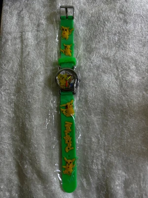Grön Pokémon klocka med Pikachu - Cool grön armbandsklocka med Pikachu-motiv och Pokémon-logga på bandet. Bandet är gjort av mjukt gummi och har flera detaljerade Pikachu-figurer i gult. Urtavlan har färgglada siffror och visare, perfekt för dig som älskar Pokémon.
