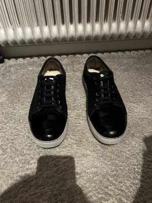 Svarta sneakers från Lanvin - Snygga svarta sneakers från Lanvin med blank tå och sidor i mocka. Skorna har rund tå, snörning och vit platt sula. Perfekt för dig som gillar stilrena och exklusiva sneakers med cool kontrast mellan material. Skorna passar till allt kontakta mig vid minsta fundering pris går att diskutera ☺️