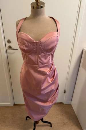Rosa satin klänning Lavish Alice - Supersnygg rosa klänning från Lavish Alice i satinliknande material. Figurnära modell med breda axelband, markerad byst och draperad kjol. Dragkedja bak för enkel påklädning. Perfekt för dig som vill sticka ut med en feminin och trendig look.