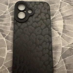 iPhone 16 mobilskal Svart Leopardmönster - Snyggt svart skal med leopardmönster, designat för iPhone 16  med tredubbla kameror. Skalet är oanvänt  och har en mjuk insida för extra skydd. Perfekt för dig som vill kombinera stil och säkerhet till din iPhone.