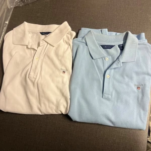 GANT pikétröjor ljusblå & vit - Två klassiska pikétröjor från GANT i storlek 170 cm, en i ljusblå och en i vit. Båda har korta ärmar, krage och knappar framtill samt GANT-logga broderad på bröstet. Perfekt för dig som gillar stilrena och tidlösa! De är i skick: 9/10, nästan precis som nya! Det är bara att skriva vid minsta lilla fråga, priset är inte hugget i sten!