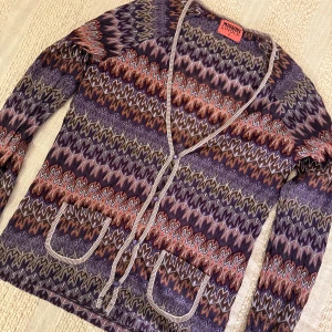 Missoni x lindex kofta 💜 - Säljer en kofta från Missoni x lindex med ikoniskt missoni i lila, orange, beige och bruna nyanser. Koftan har v-ringning, två fickor fram och stängs med små pärlknappar. Materialet är mjukt och stretchigt, perfekt för lager-på-lager. Superfin till jeans eller kjol!