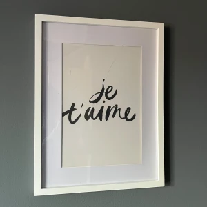 Tavlor - Bilderna visar två inramade konsttryck med vita ramar. Ena motivet är texten 'je t'aime', det andra en minimalistisk linjeteckning av en sittande kvinna. Passepartouten har synliga veck/skador i hörnen, men ramarna är i gott skick. Perfekt för modern inredning. Vill man köpa som separat så e de 50kr styck.