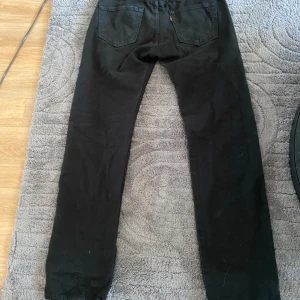 Svarta Levi's 501 jeans W30 L32 - Svarta klassiska Levi's 501 jeans med raka ben och femficksmodell. Jeansen har den ikoniska läderpatchen bak i midjan och är tillverkade i robust bomullsdenim. Perfekta för dig som gillar en tidlös och clean look.