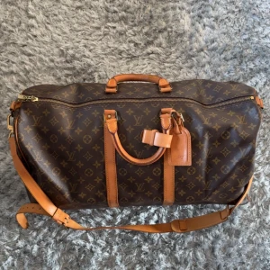 Louis Vuitton Keepall 55 Monogram - Louis Vuitton Keepall 55 i klassiskt monogrammönster med bruna och beige färger. Väskan har detaljer i skinn, justerbar axelrem, dubbla handtag och dragkedja. Perfekt för resor och weekendtrips, ikonisk design med LV-logga över hela väskan.